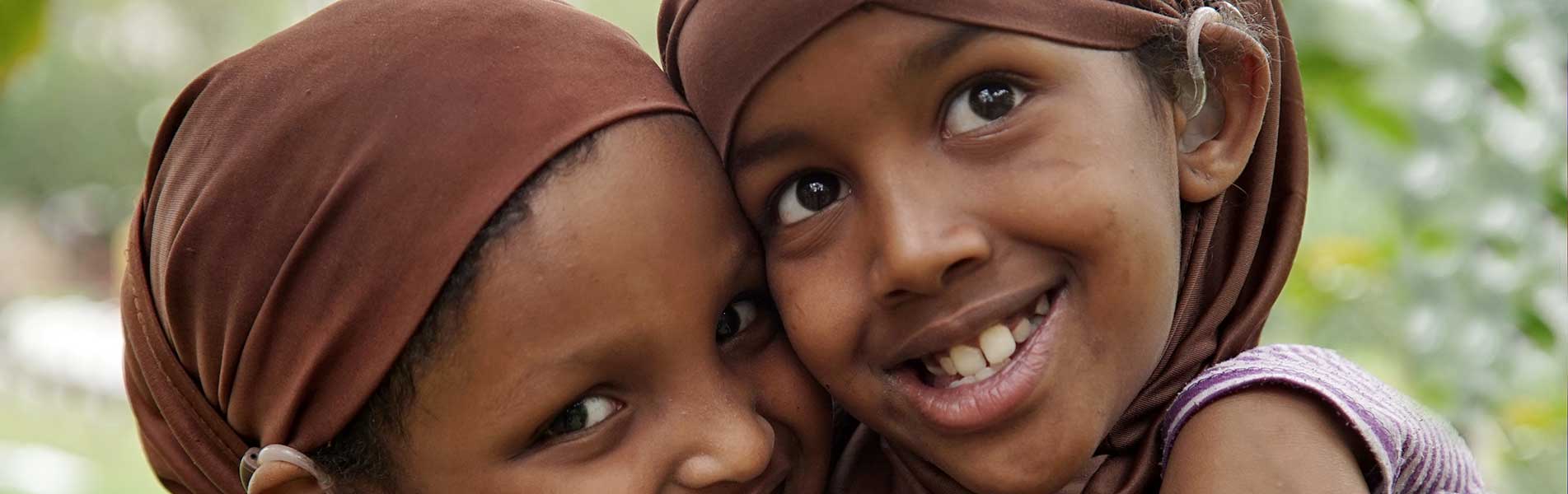 two girls in Nairobi hugging and happy with their hearing aids