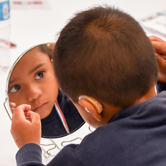 little boy trying on hearing aid in a mirror