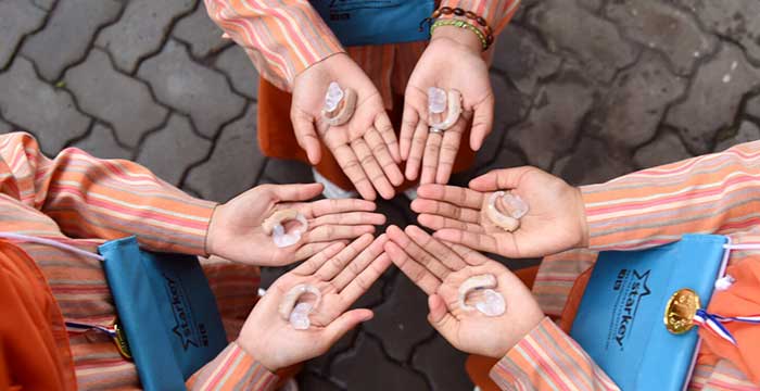 6 hands holding hearing aids